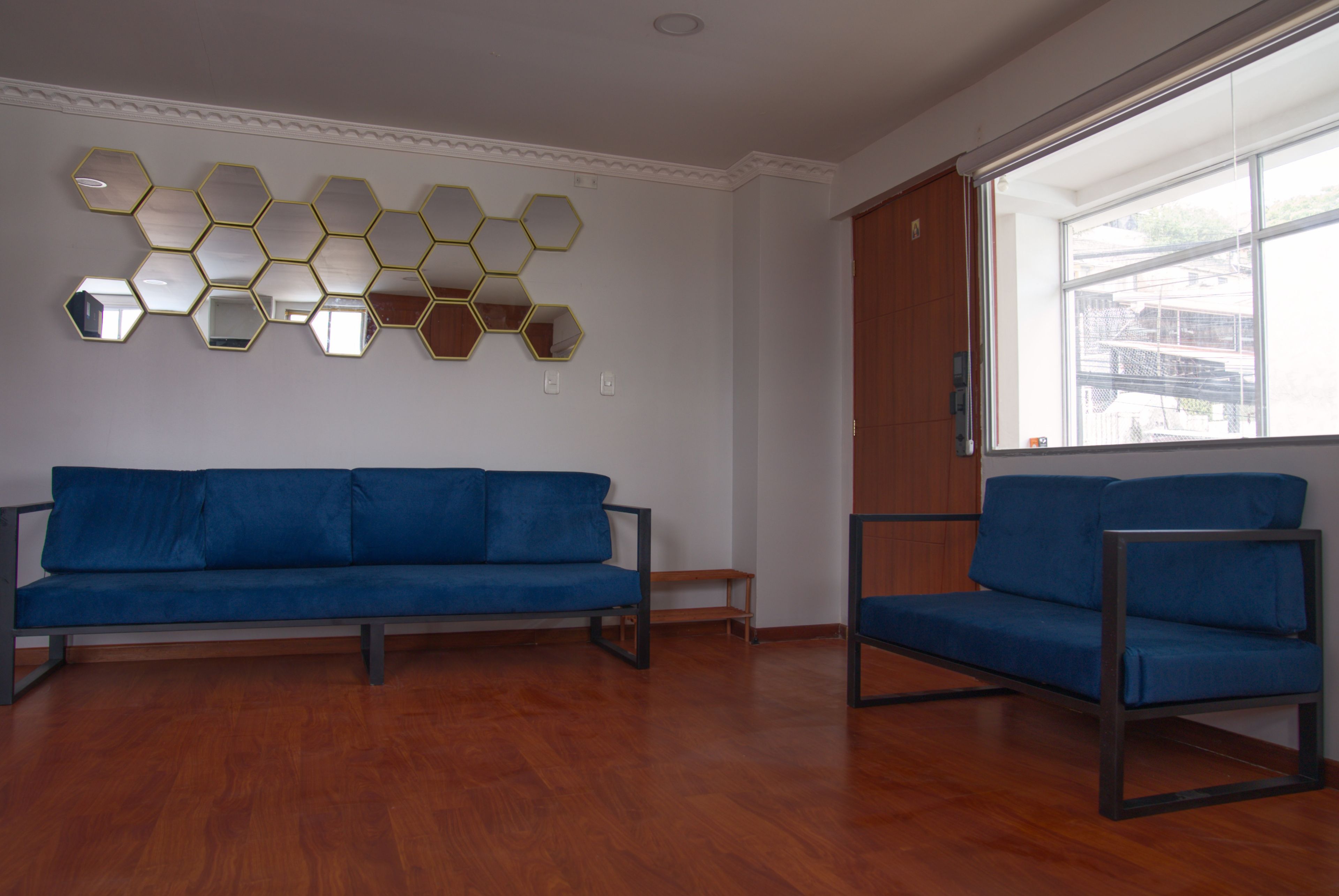 A room with a blue sofa, a smaller blue chair, and a wall with hexagonal mirrors.