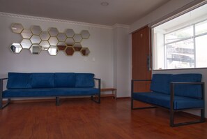 A room with a blue sofa, a smaller blue chair, and a wall with hexagonal mirrors.