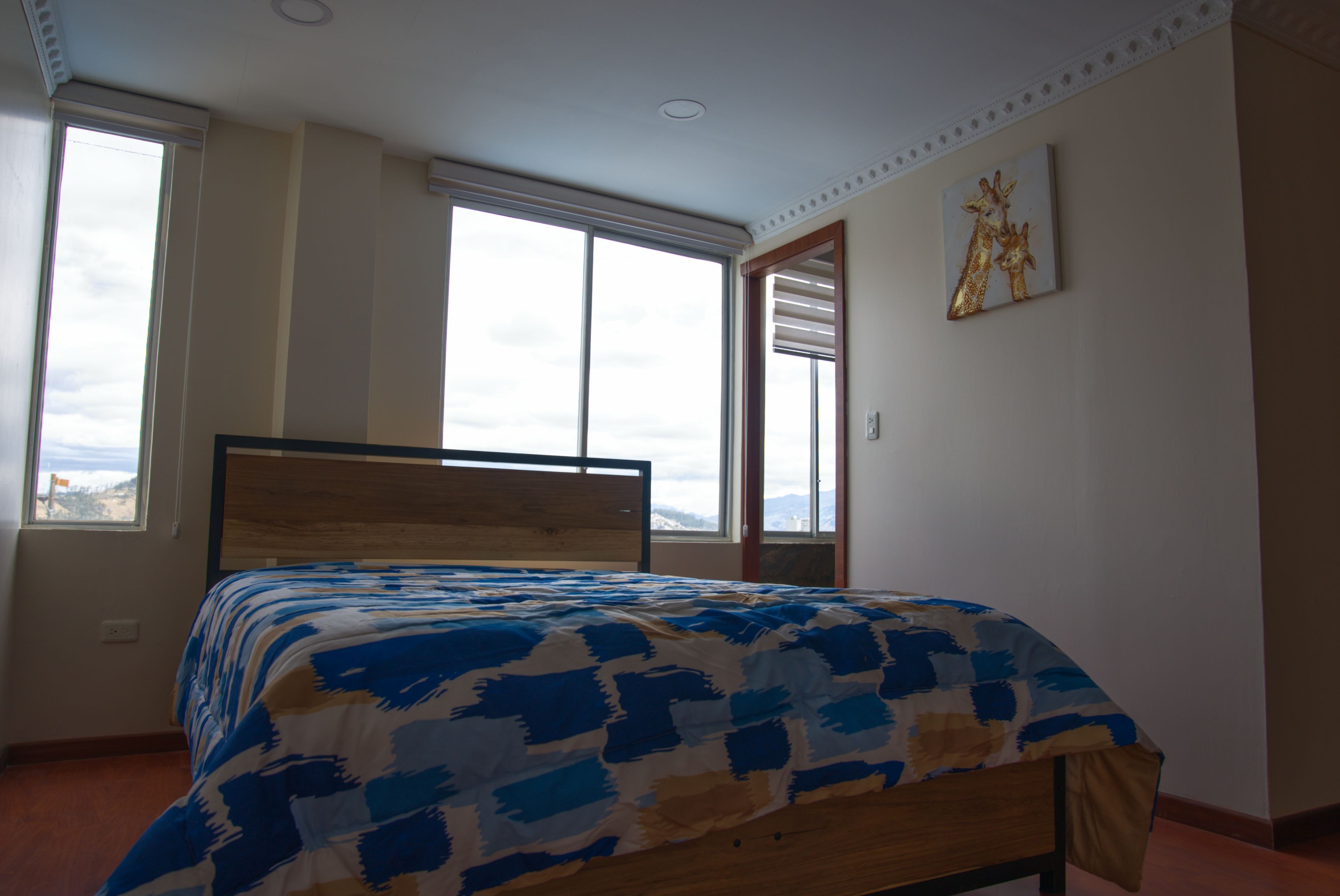 A bedroom with a bed, large windows, and a painting on the wall.