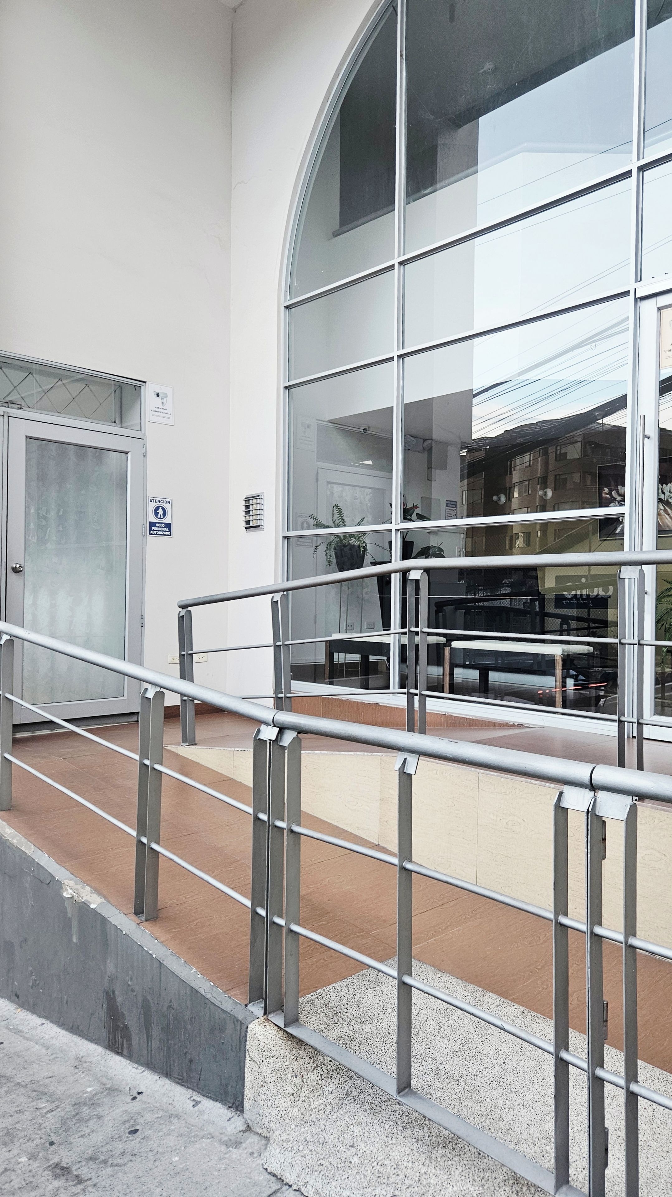 A modern building with a large glass facade, metal railings, and a tiled floor.