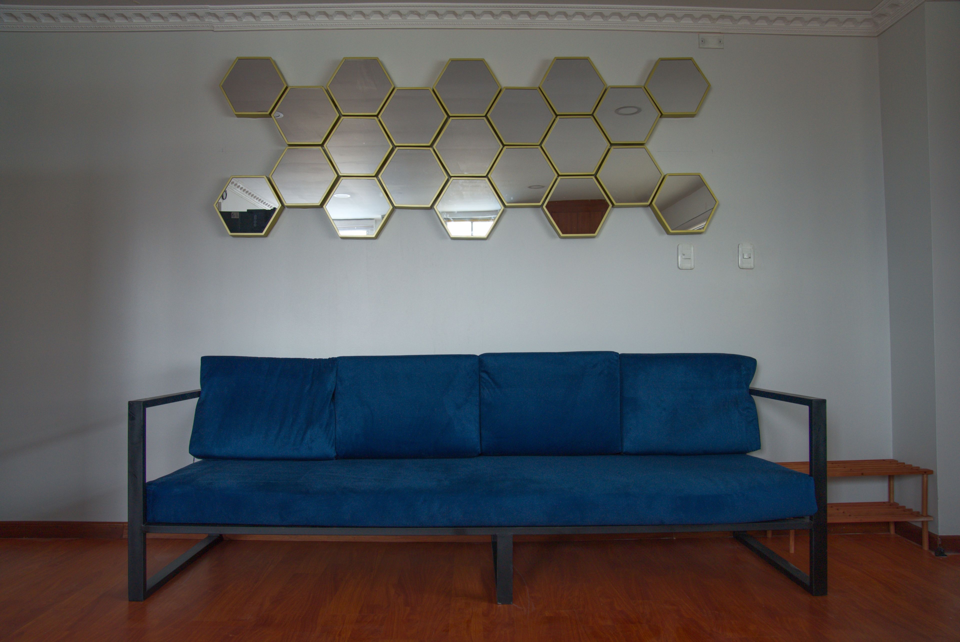 A room with a blue sofa, a wall-mounted hexagonal mirror arrangement, and a wooden floor.