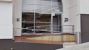 A modern building entrance with a glass facade, metal railings, and a concrete ground.