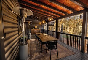 Una terraza de madera con una mesa y sillas, un calentador grande y vistas a árboles.
