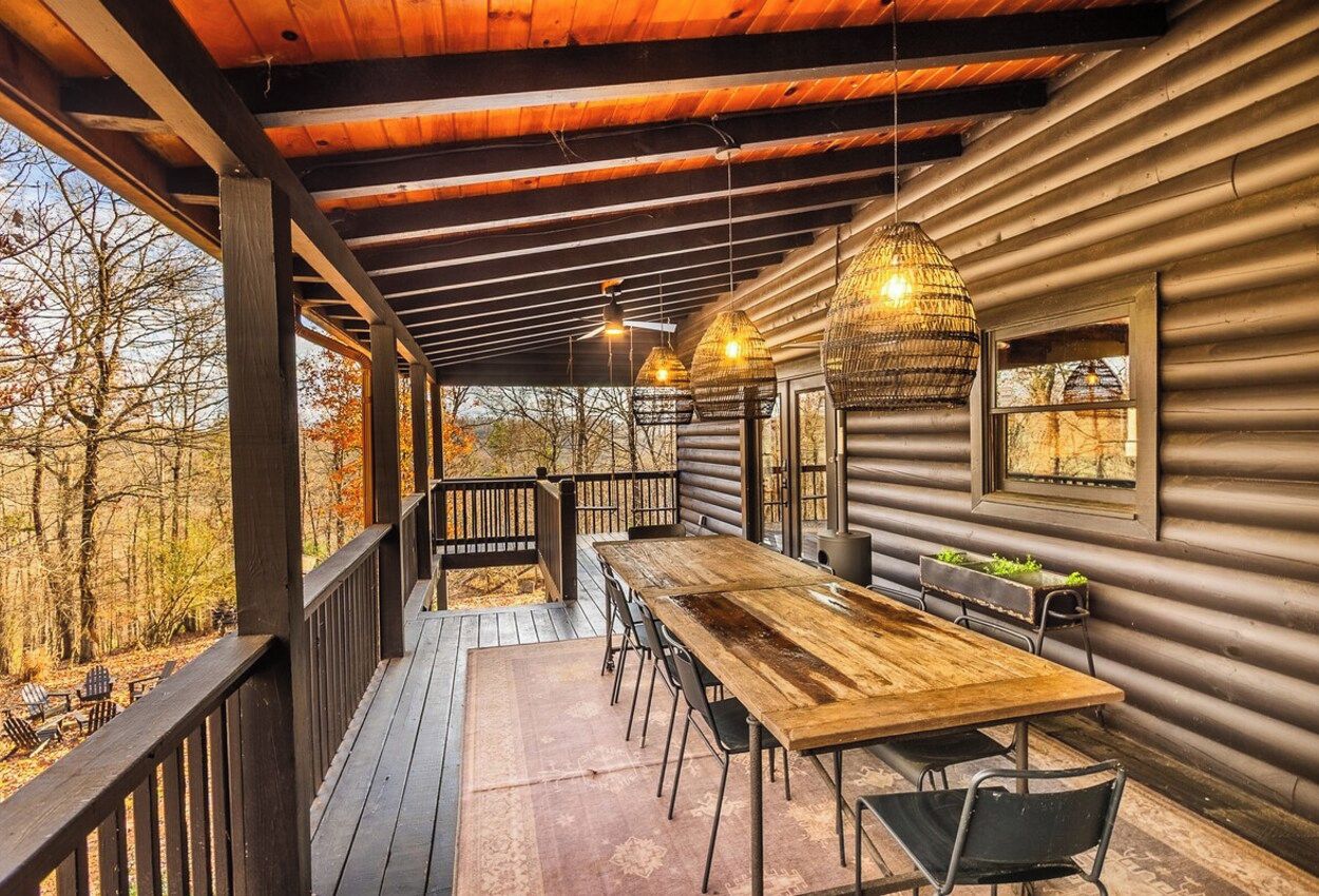 Une terrasse en bois avec une table et des chaises, un luminaire suspendu et une fenêtre donnant sur les arbres.