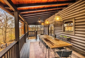 Una terraza de madera con una mesa y sillas, una lámpara colgante y un ventanal con vistas a árboles.