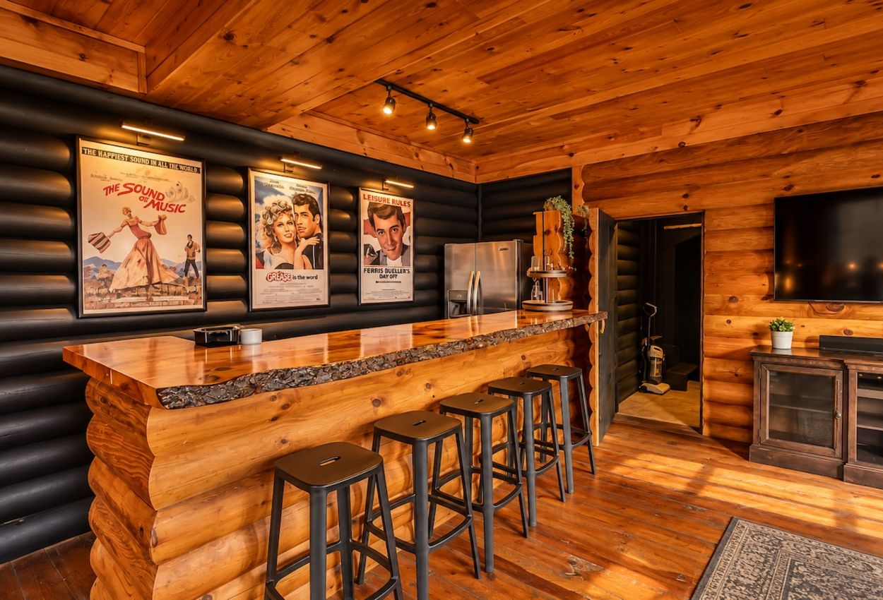 A log cabin interior with a bar area, wooden walls, and a large TV.