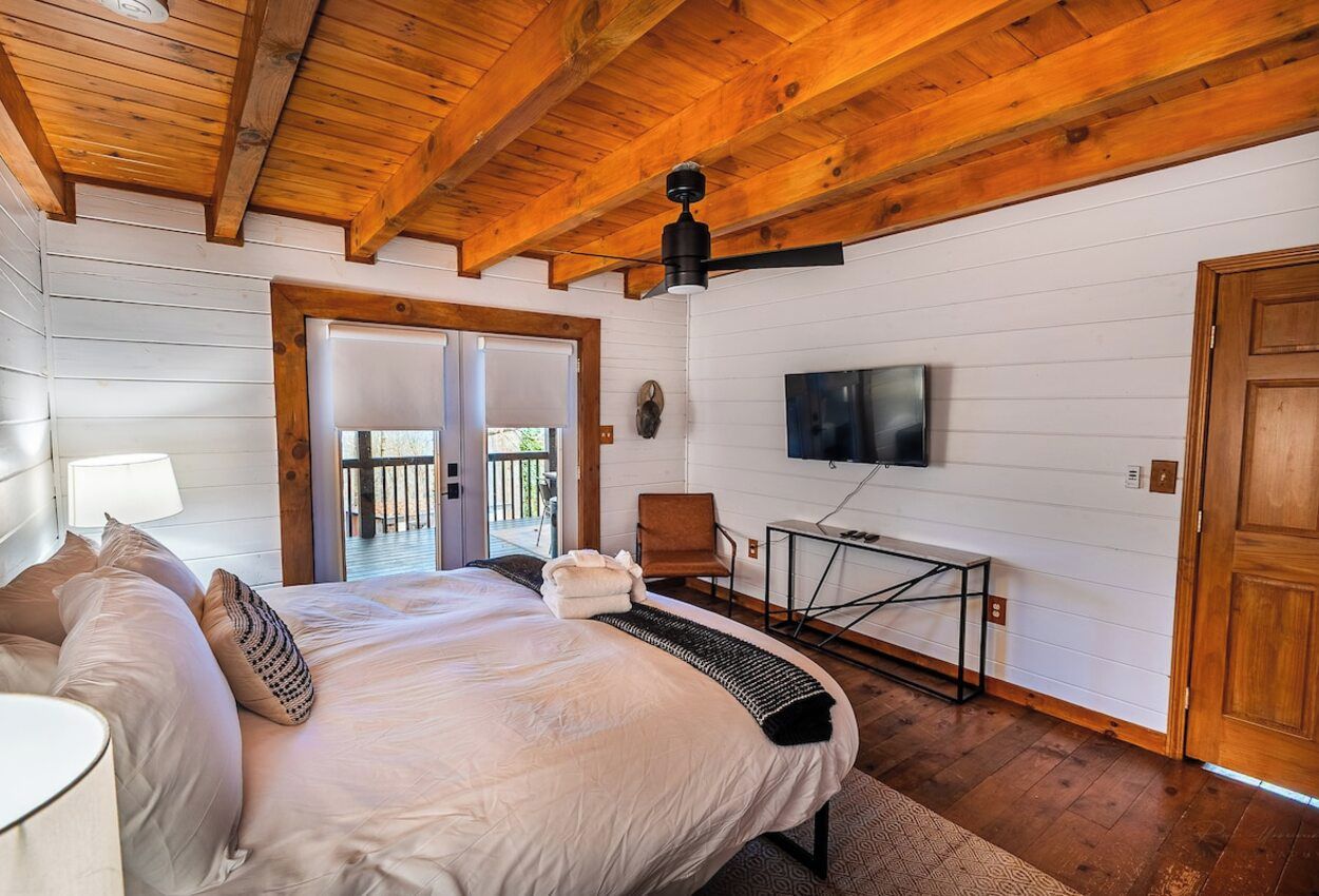 A bedroom with a bed, a television, a chair, and a table.