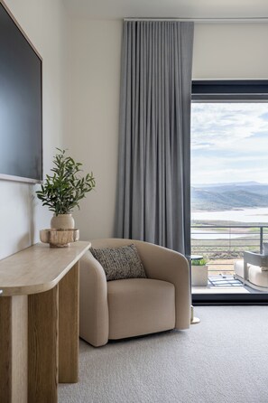 En moderne stue med sofa, sofabord, en potteplante og udsigt over et landskab gennem store vinduer.