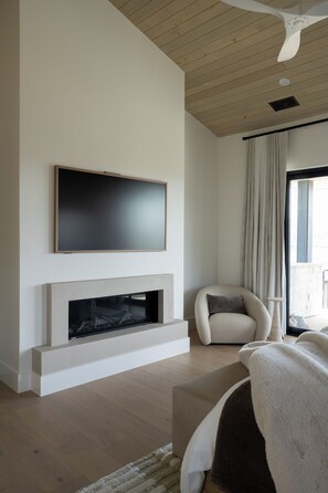 A modern living room with a flat-screen TV mounted above a fireplace, a comfortable armchair, and a large window with curtains. - Deer Valley East Village - Mountain Views - Sleeps 12 4B/5.5B - Ski in Minutes (Daniel)