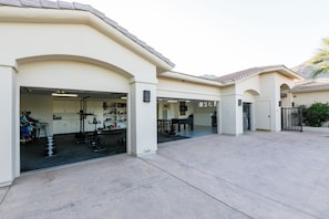 A residential building with a garage containing exercise equipment and a dining area. - Desert Paradise: Waterslide, Pickleball, Basketball, Game Room, & Gym! (Palm Desert)