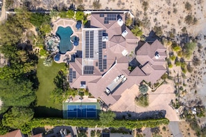Luchtbeeld van een woonhuis met zwembad, zonnepanelen en een tennisbaan.