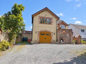 A two-story building with a prominent wooden garage door, a brick chimney, and a gravel driveway. - Ty Cerrig Bach – Hot tub, games room & pet-friendly stay near Benllech (Tyn-y-Gongl)