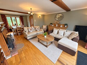 A living room with a sofa, coffee table, and dining area. - Ty Cerrig Bach – Hot tub, games room & pet-friendly stay near Benllech (Tyn-y-Gongl)