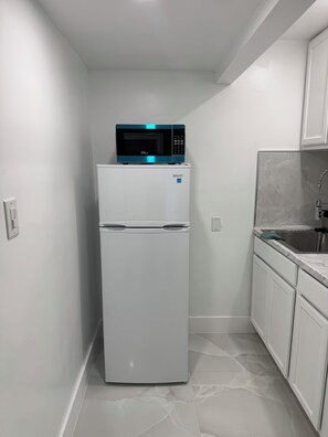 Une cuisine compacte avec un réfrigérateur blanc, un four à micro-ondes placé sur le dessus et un évier doté d’un plan de travail en marbre.