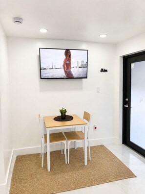 Un intérieur moderne avec un téléviseur à écran plat fixé au mur, une petite table avec des chaises et une porte dotée d’un cadre noir.