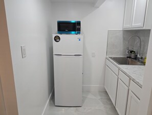 Une cuisine de taille réduite, avec un réfrigérateur blanc, un four à micro-ondes et un évier.