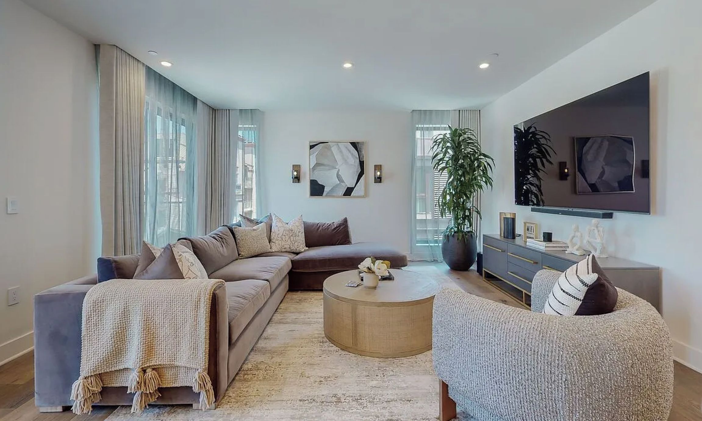 A modern living room with a sectional sofa, a round coffee table, and a TV mounted on the wall.