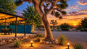 A covered outdoor seating area with tables and chairs, a large tree, and a sunset in the background. - Casa Sol, Fire Pit, Games, BBQ, Stargazing, More (Yucca Valley)