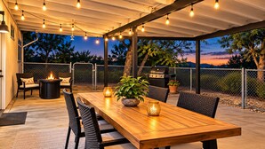 An outdoor patio with a wooden table, chairs, a fire pit, and string lights. - Casa Sol, Fire Pit, Games, BBQ, Stargazing, More (Yucca Valley)