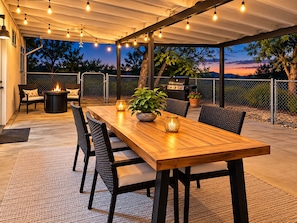 An outdoor patio with a wooden table, chairs, a fire pit, and string lights. - Casa Sol, Fire Pit, Games, BBQ, Stargazing, More (Yucca Valley)