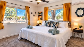 A bedroom with a bed, two bedside tables, a ceiling fan, and a large window with curtains. - Casa Sol, Fire Pit, Games, BBQ, Stargazing, More (Yucca Valley)