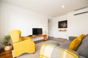 A modern living room with a yellow armchair, a grey sofa, a flat-screen TV, and a painting on the wall. - Top floor apartment in city center (Funchal)