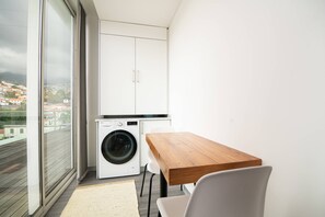 A compact kitchen with a washing machine, a wooden table, and a view of a cityscape through large windows. - Top floor apartment in city center (Funchal)