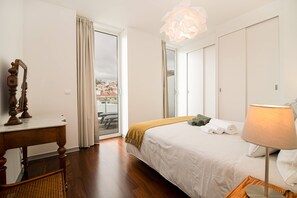 A hotel room with a bed, a desk, a chair, a lamp, and a view of a cityscape through the window. - Top floor apartment in city center (Funchal)