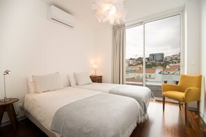 Een hotelkamer met twee bedden, een stoel, een lamp en uitzicht op de stad.