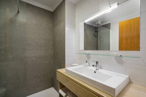 A modern bathroom with a glass shower enclosure, a white sink, and a mirror with a wooden panel. - City Center Boutique (Funchal)