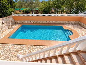 A rectangular swimming pool with a stone border, surrounded by a white railing and a staircase leading up to it. - Villa family AR (Denia)