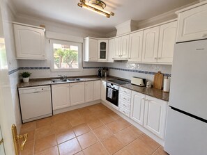 A kitchen with white cabinetry, a built-in oven, a sink, and a window. - Villa family AR (Denia)
