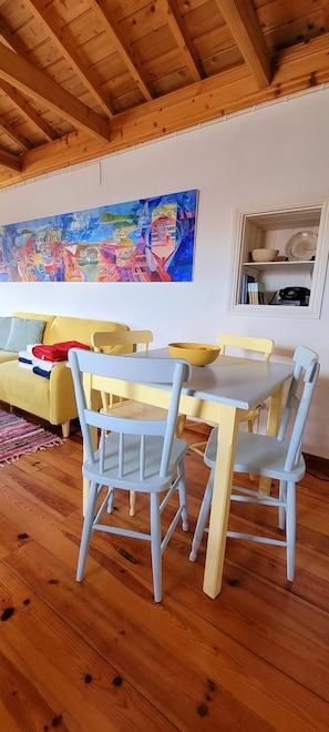 Ein Essbereich mit Holzbalkendecke, einem Gemälde an der Wand und einem gelben Sofa.