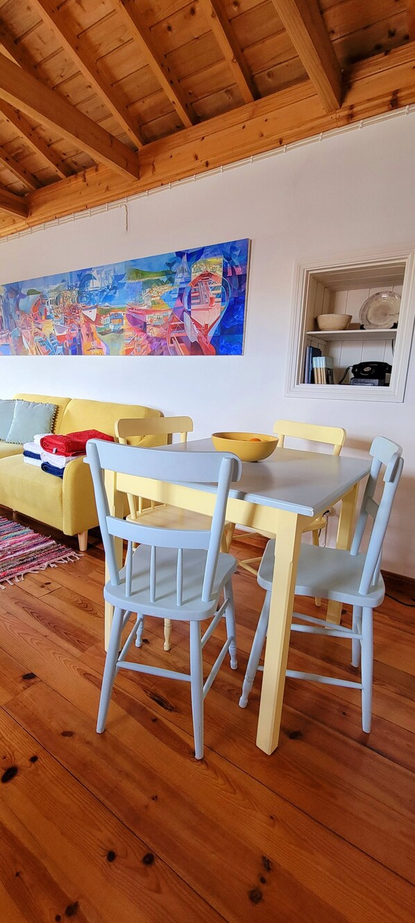 A dining area with a wooden ceiling, a painting on the wall, and a yellow sofa.