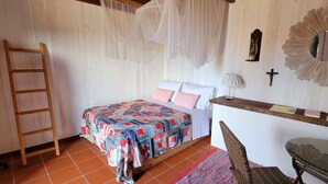 A bedroom with a bed, a wooden ladder, a chair, a desk with a mirror, and a cross on the wall. - Casa do Cachorro – Adega Chamarrita (Madalena (Açores))