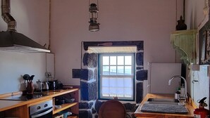 A kitchen with a stone wall, wooden cabinets, a stove, and a window. - Casa do Cachorro – Adega Chamarrita (Madalena (Açores))