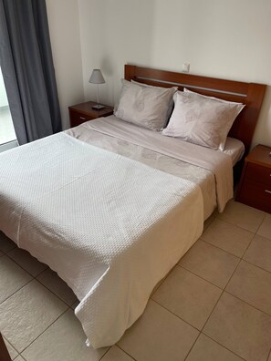 A neatly made bed with a patterned bedspread, a wooden headboard, and two bedside tables with lamps. - Vila Baleira Apartment (Porto Santo)