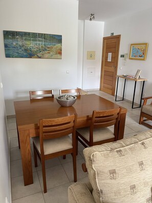 A dining area with a wooden table and chairs, a bowl on the table, and a painting on the wall. - Vila Baleira Apartment (Porto Santo)