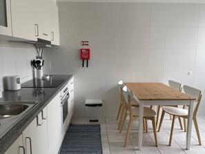 A modern kitchen with a wooden table and chairs, a stainless steel sink, and a fire extinguisher on the wall. - Vila Baleira Apartment (Porto Santo)