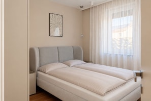 Ein Schlafzimmer mit einem Bett, einem Nachttisch, einer Wandleuchte und einem Fenster mit durchsichtigen Vorhängen.