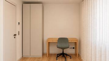Een kamer met een houten bureau, een grijze bureaustoel, een kledingkast en een raam met gordijnen.