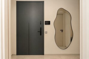 Eine moderne Tür mit Griff und Schlüsselloch, ein kleines elektronisches Gerät an der Wand und ein großer, unregelmäßig geformter Spiegel.