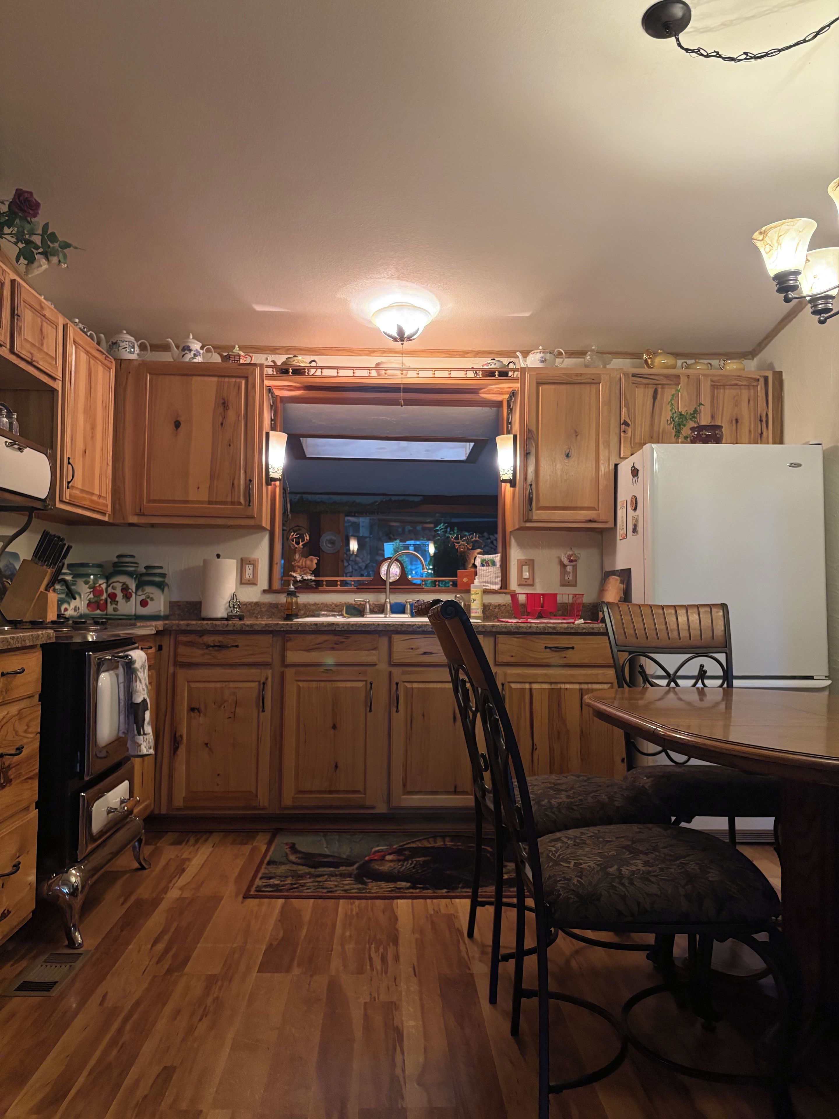 A kitchen with wooden cabinets, a refrigerator, a dining table with chairs, and a chandelier.