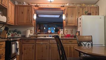 A kitchen with wooden cabinets, a refrigerator, a dining table with chairs, and a chandelier.