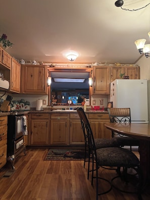 Uma cozinha com armários de madeira, geladeira, mesa de jantar com cadeiras e um lustre.