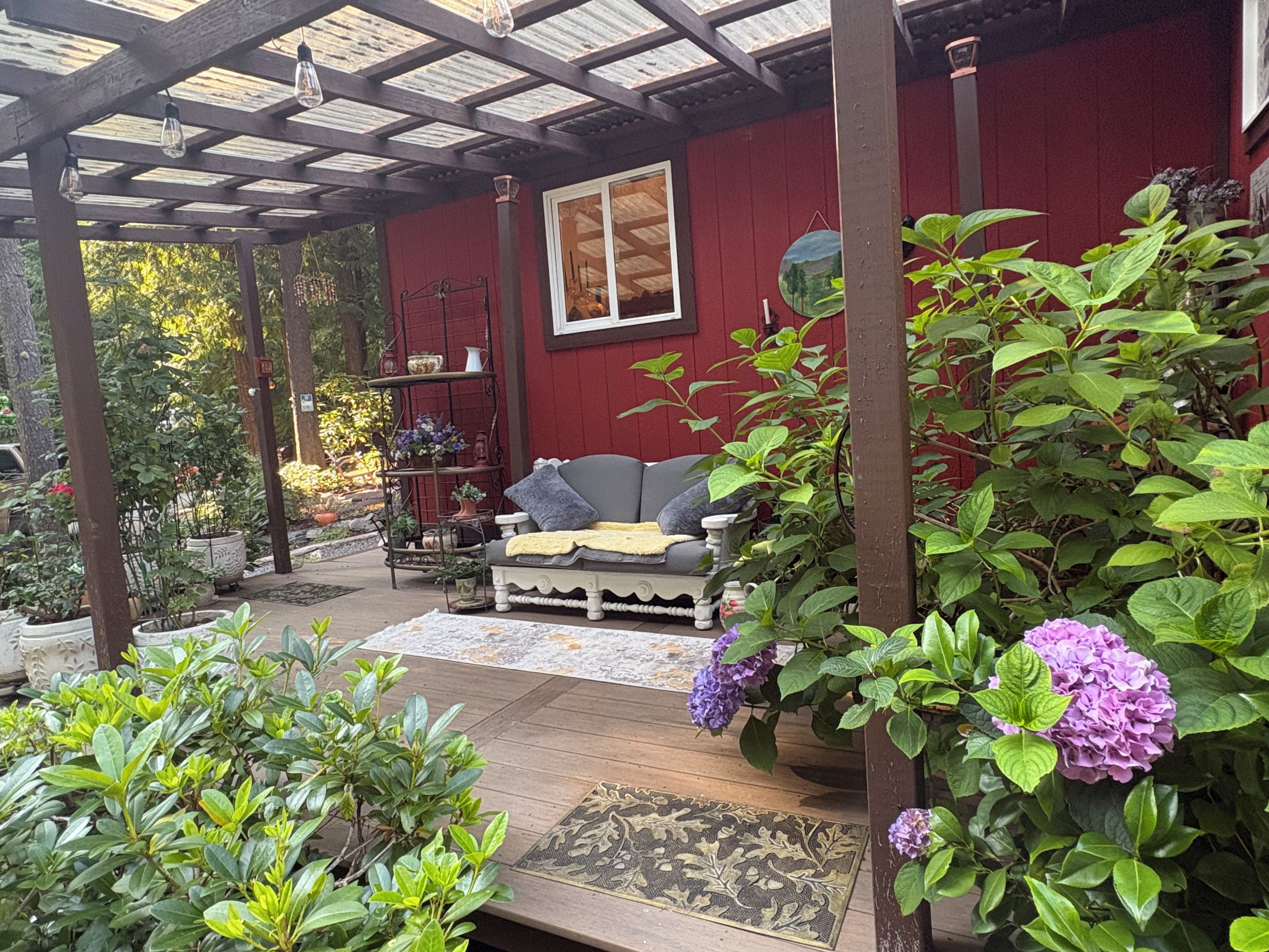 Un patio cubierto con un banco de madera, pared roja y plantas en macetas.