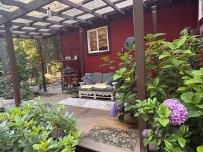 A covered patio area with a wooden bench, a red wall, and potted plants.