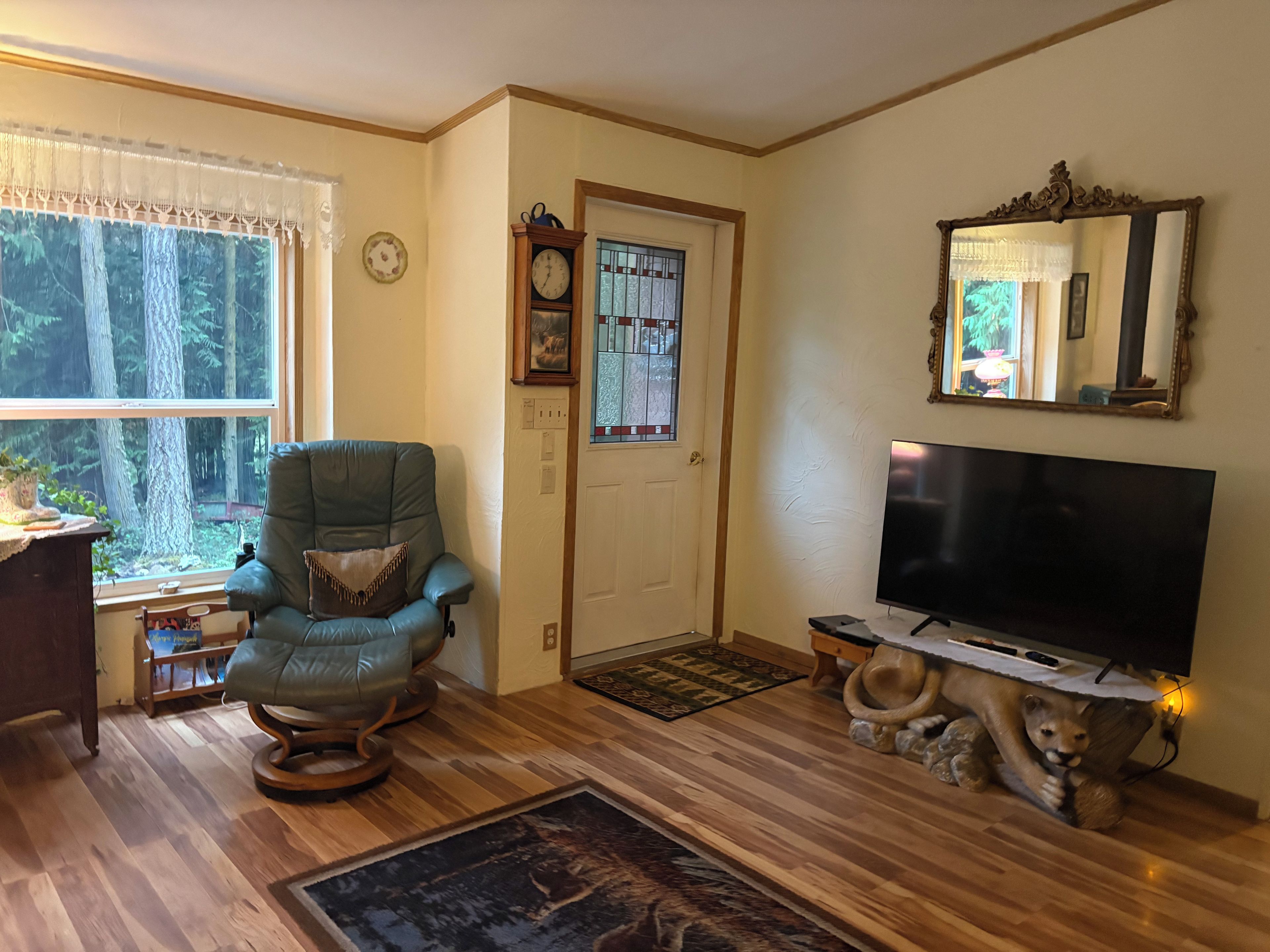 A living room with a large flat-screen TV, a rocking chair, a wooden coffee table, and a door with a stained glass window.