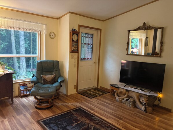 A living room with a large flat-screen TV, a rocking chair, a wooden coffee table, and a door with a stained glass window.