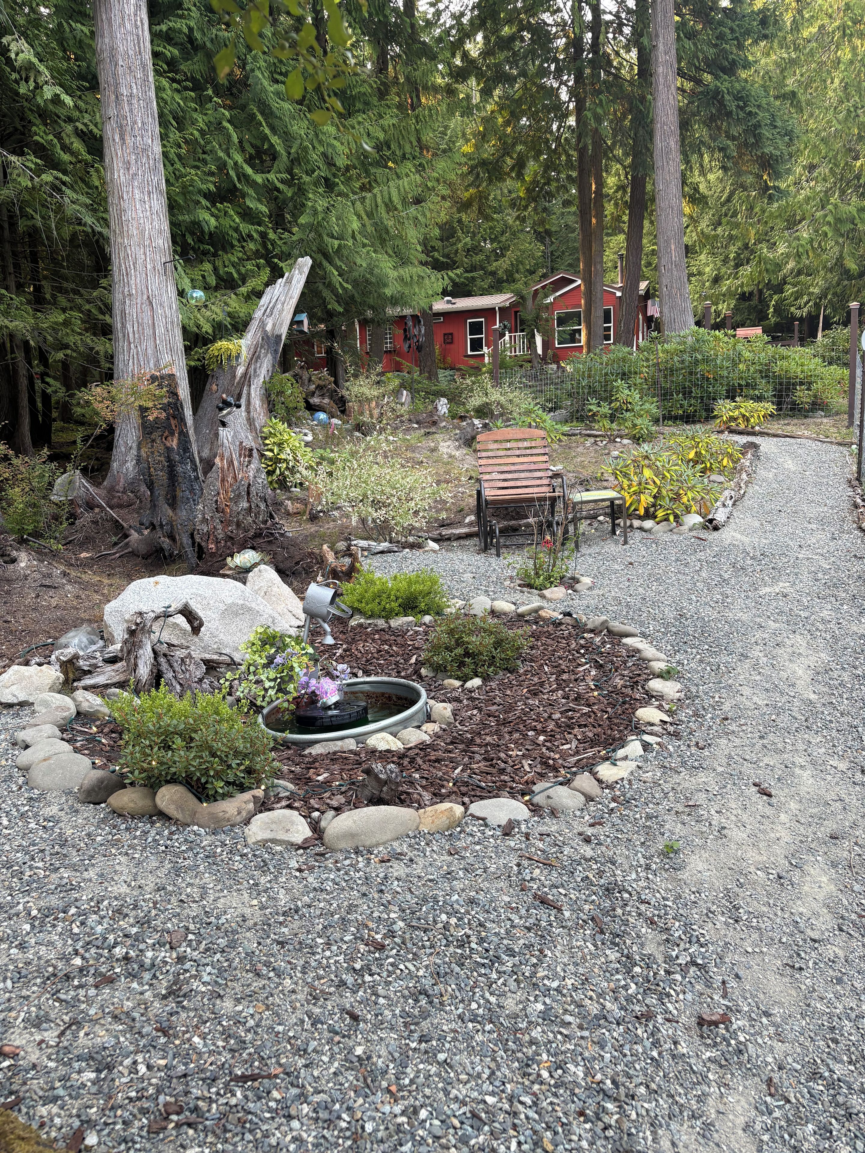 A garden with a gravel path, a wooden bench, and a small pond.